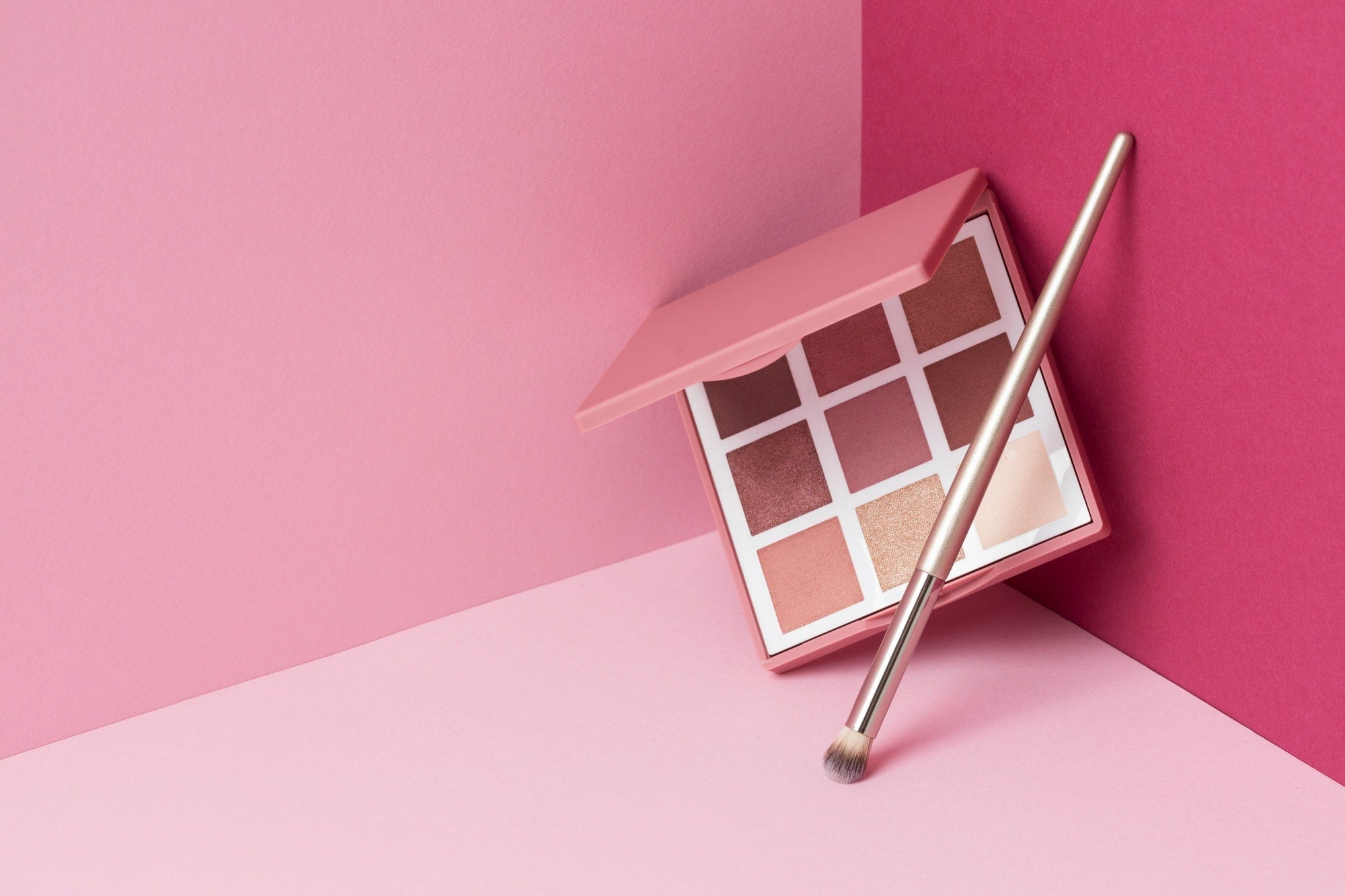 Eyeshadow palette with makeup brush on pink background, professional makeup tools